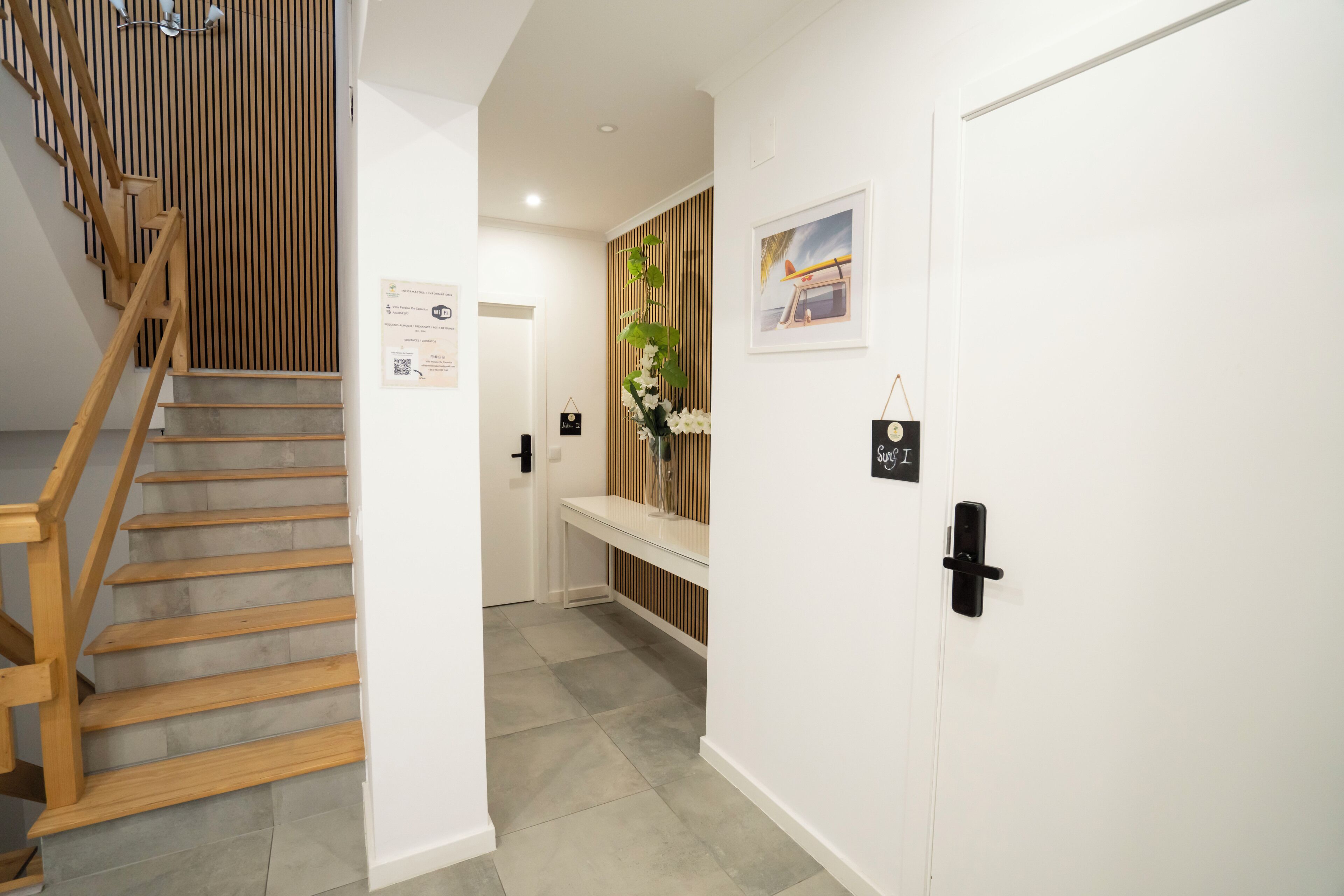 Un couloir d’hôtel moderne avec un escalier en bois, un comptoir d’accueil et une porte portant une enseigne.