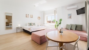 A modern hotel room with a bed, a sofa, a round table, and a TV mounted on the wall. - Villa Paraiso Da Caparica (Almada)
