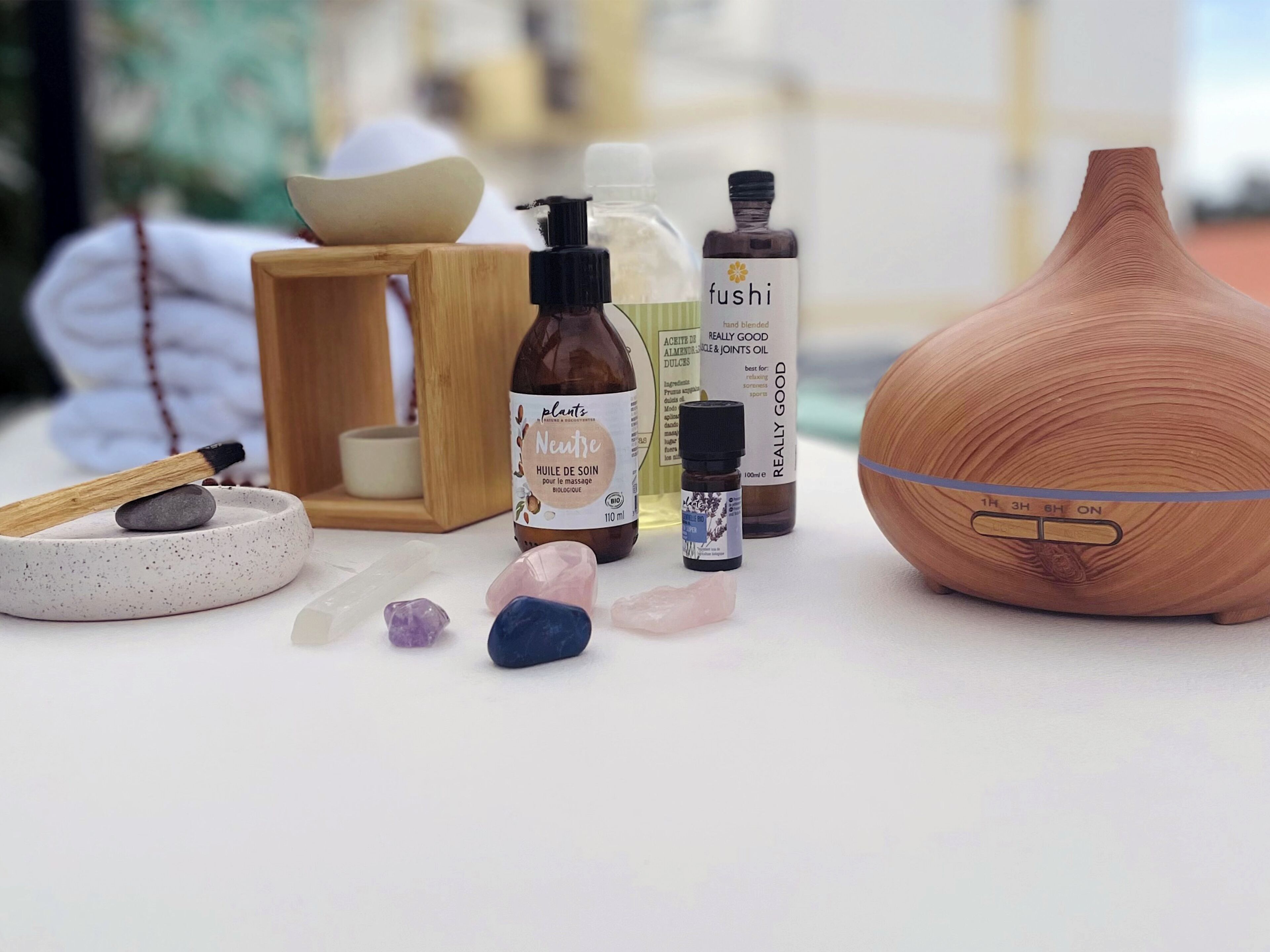 Una botella de aceite de masaje, un difusor, un cuenco de madera y algunas piedras sobre una mesa.