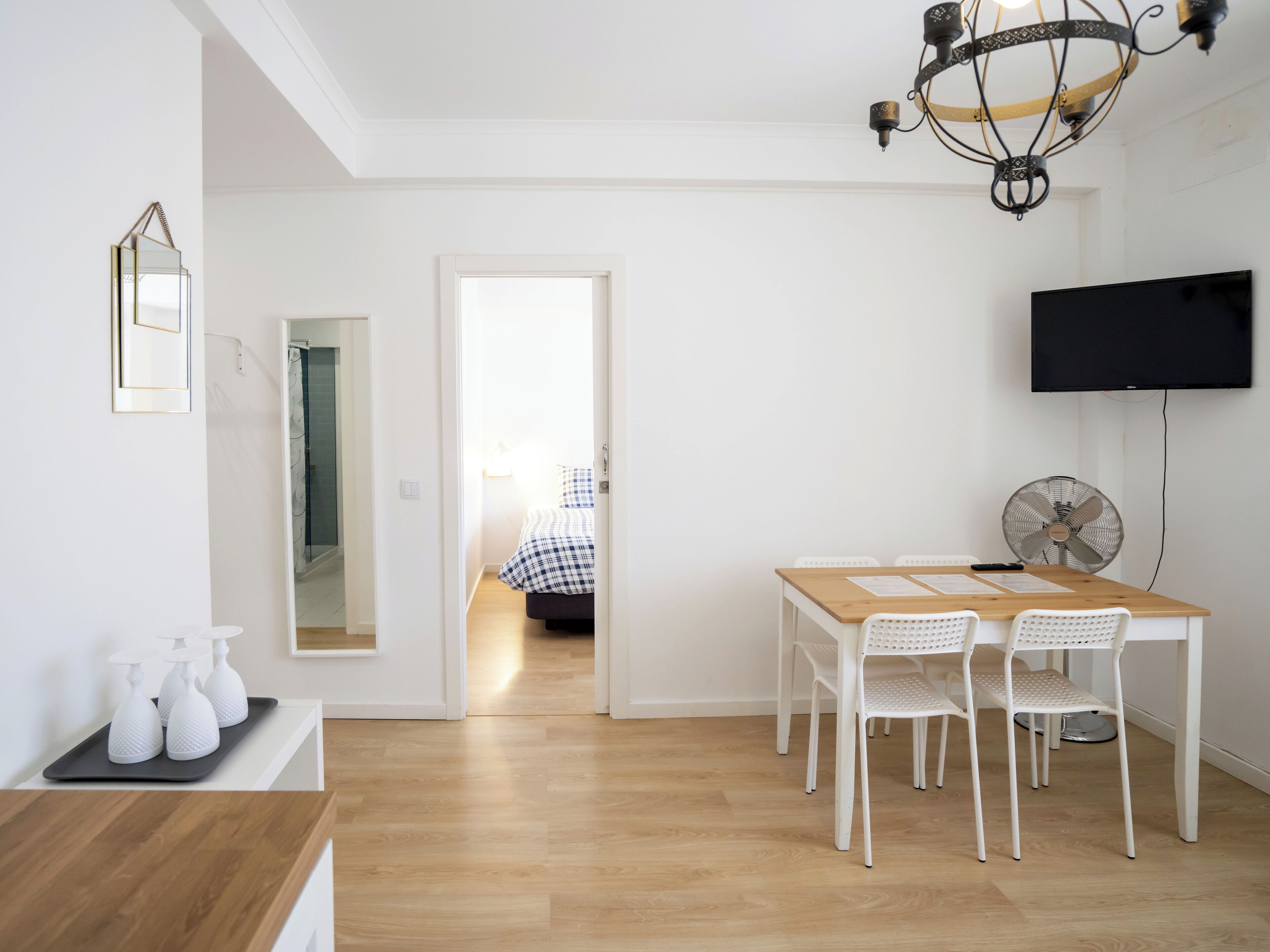 Un'area pranzo moderna con tavolo in legno, sedie bianche, un televisore a schermo piatto montato a parete e una ventola a soffitto.