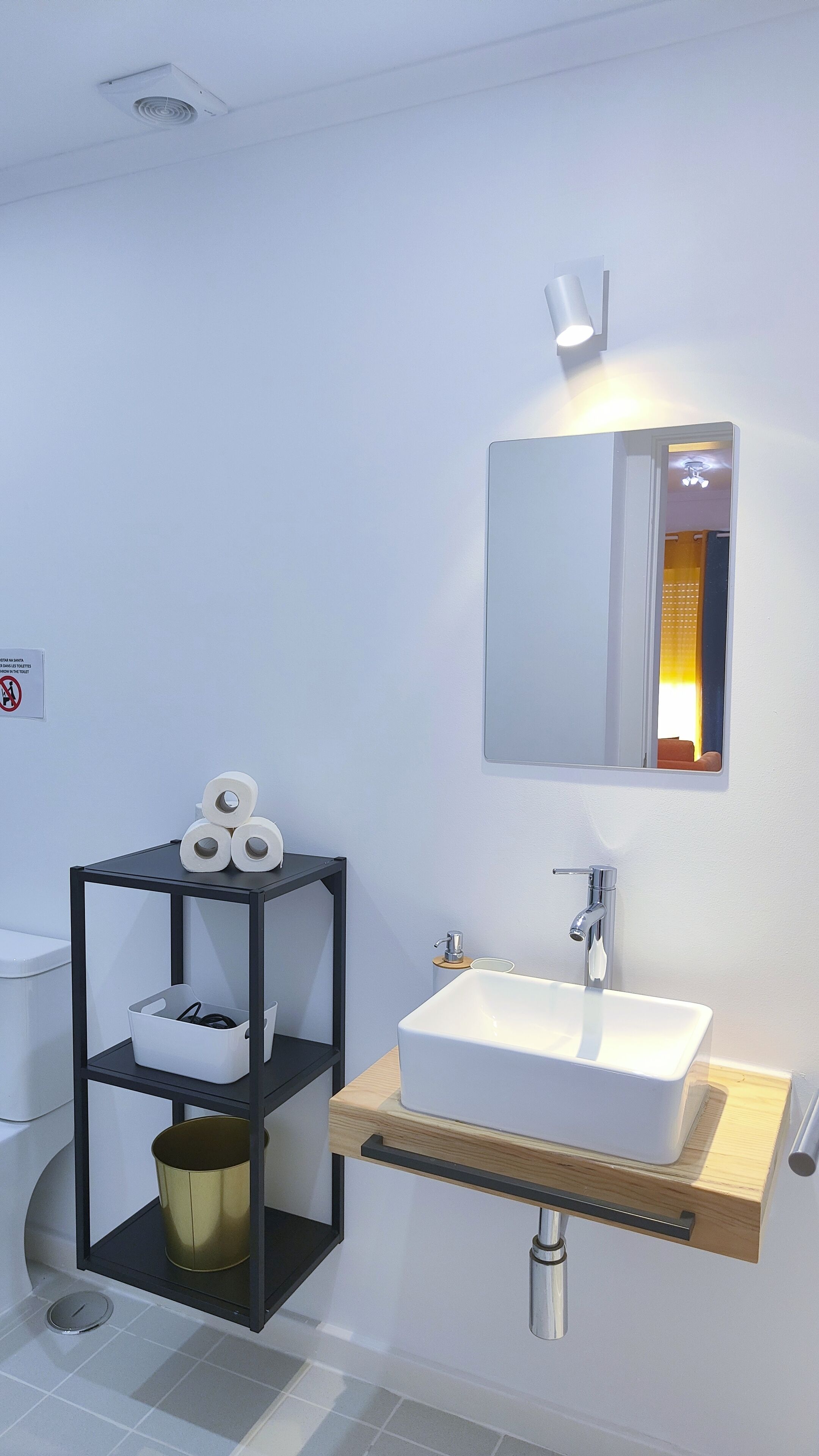 A modern bathroom with a white sink, a mirror, a shelf with toiletries, and a toilet.