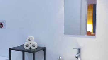 A modern bathroom with a white sink, a mirror, a shelf with toiletries, and a toilet.