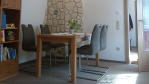 Una habitación con pared de piedra, techo de madera, una mesa con sillas, una estantería y una puerta.