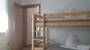 Una habitación con literas, una cama individual, suelo de madera, una puerta y una ventana con cortinas.
