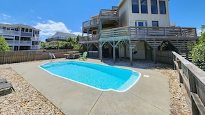 Una casa de dues plantes amb piscina, terrassa de fusta i pati tancat per una tanca.