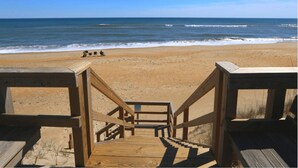 Una passera de fusta que condueix a una platja amb cel blau i aigües tranquil·les.