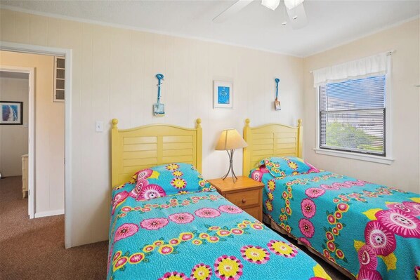 Un dormitorio con dos camas, cada una con colcha estampada, una mesita de noche con lámpara y una ventana con persianas.