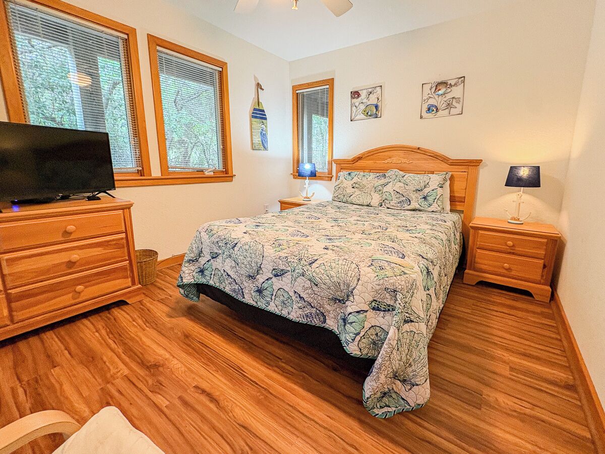 A bedroom with a bed, a dresser, a TV, and a window with blinds.