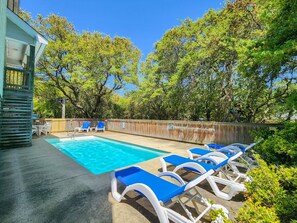 A swimming pool with blue and white lounge chairs, surrounded by trees and a wooden fence.