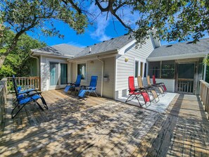 A covered deck with multiple lounge chairs, a wooden deck, and a house with a grey roof.