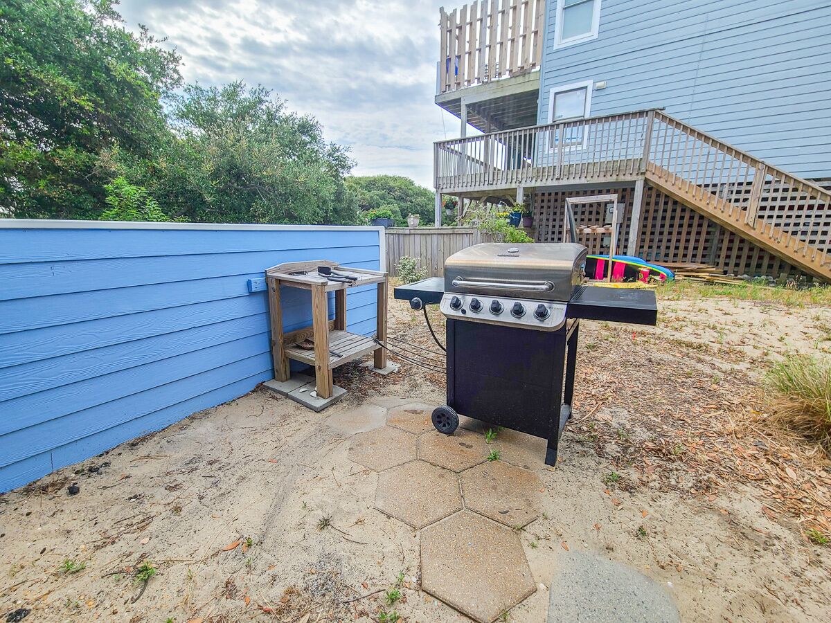 A backyard with a barbecue grill, a wooden deck, and a blue house.