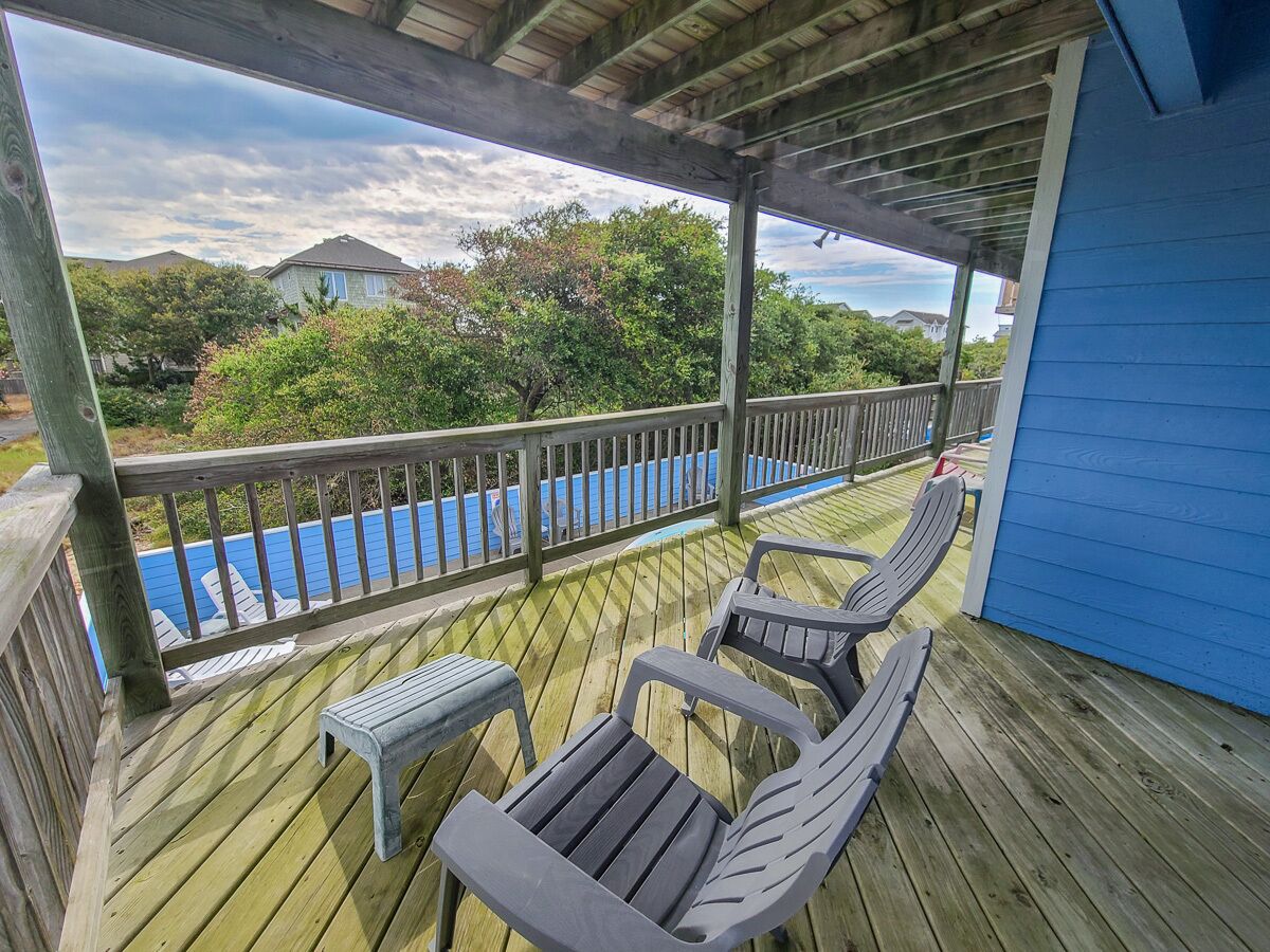 Eine Holzterrasse mit zwei Stühlen und einem kleinen Tisch, mit Blick auf einen Swimmingpool und eine Wohngegend.