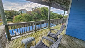 Une terrasse en bois avec deux chaises et une petite table, donnant sur une piscine et un quartier résidentiel.