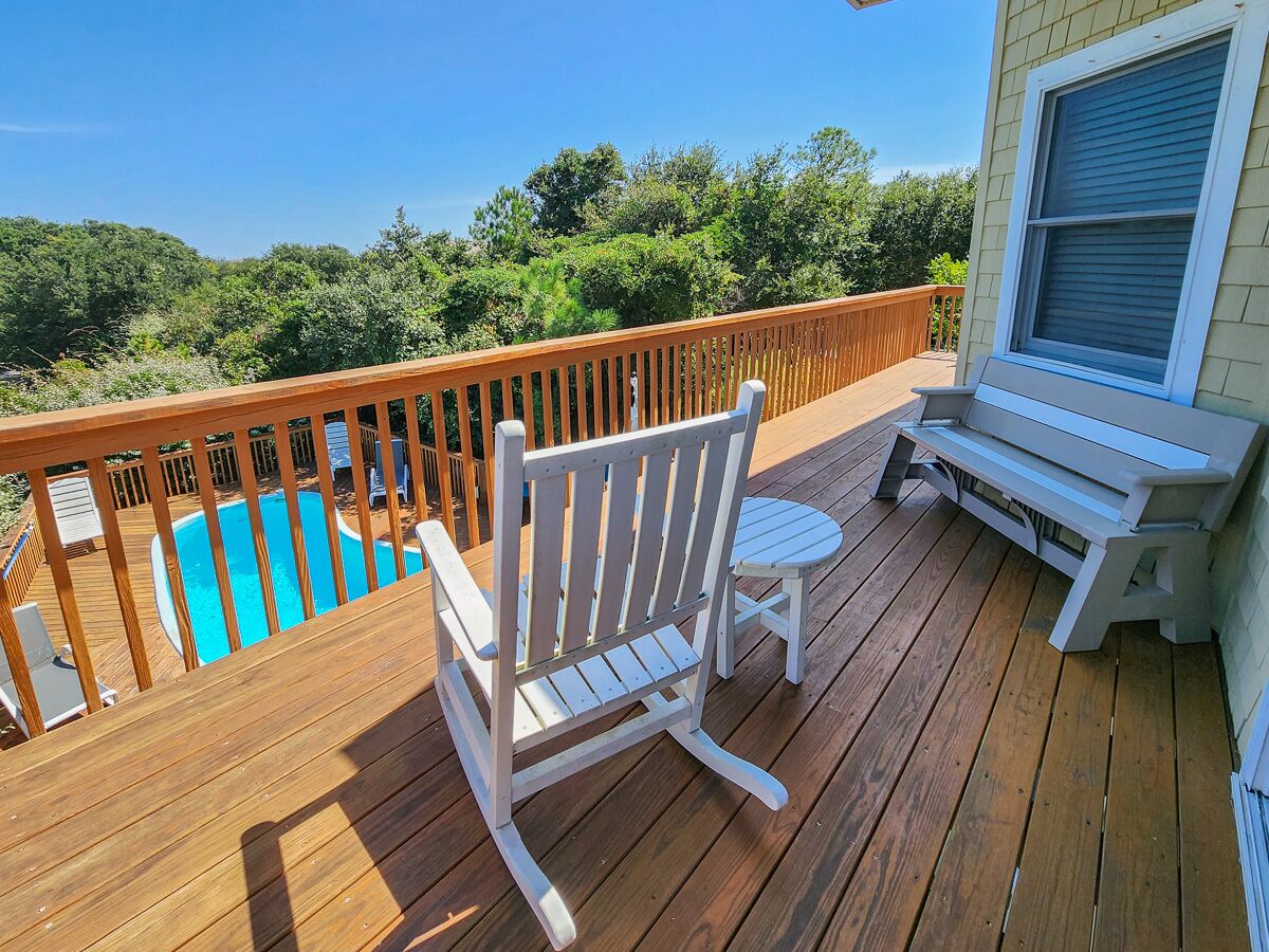 Une terrasse en bois avec une piscine, une chaise Adirondack blanche et une petite table.