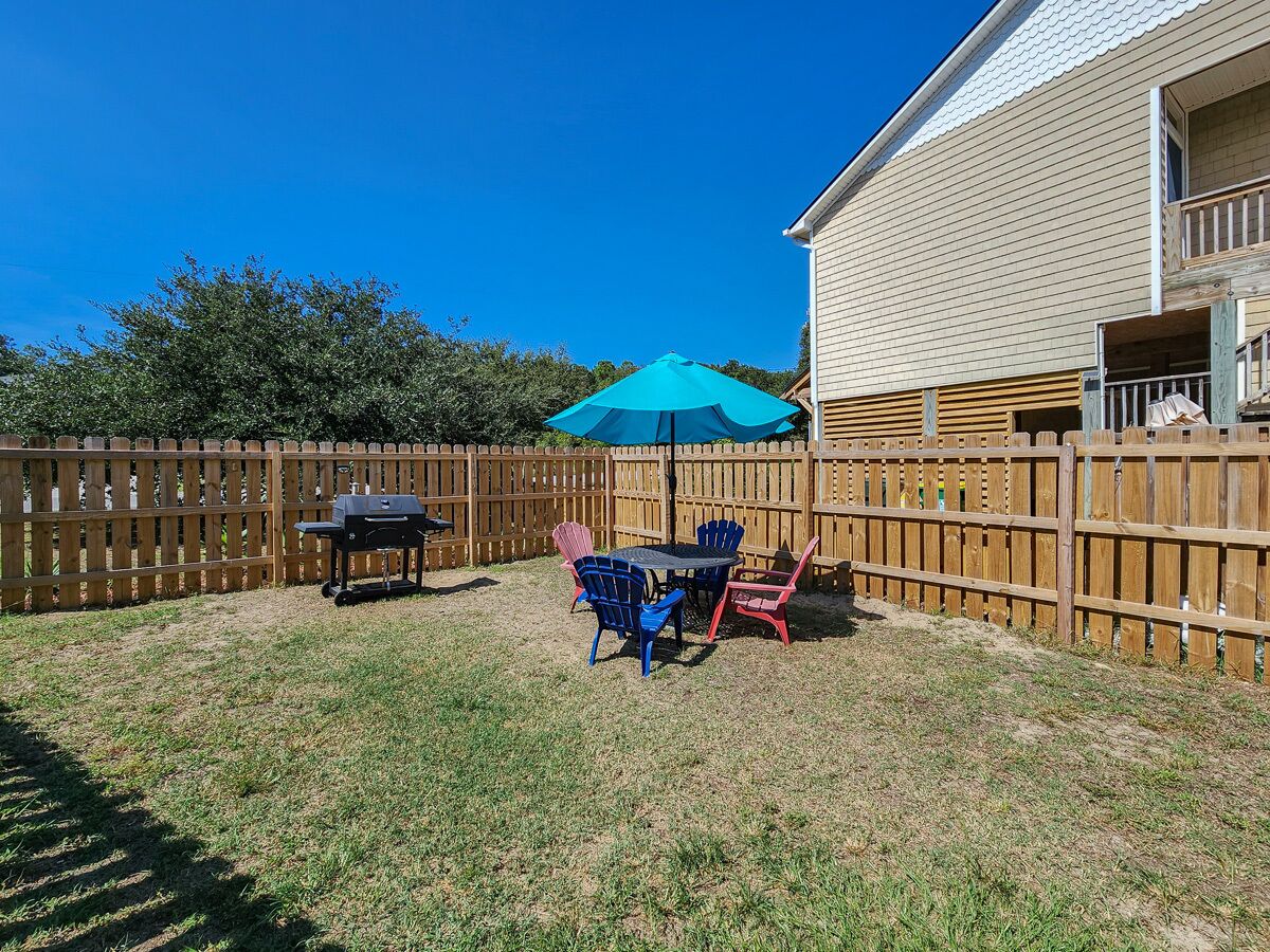 A backyard with a wooden fence, a barbecue grill, and a table with chairs.