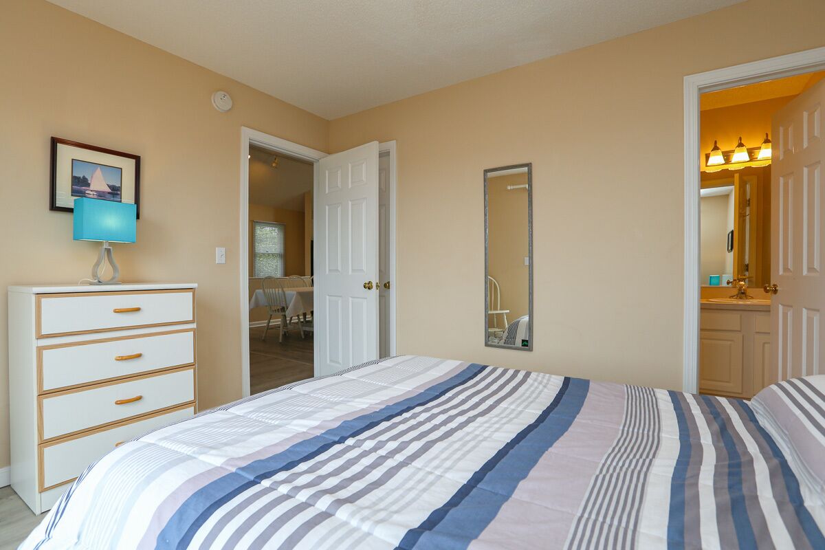 A bedroom with a bed, a dresser, a mirror, and a door leading to a bathroom.