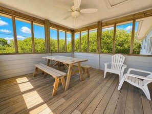 Un espace extérieur abrité, doté d’une terrasse en bois, d’une table avec des bancs et de deux fauteuils Adirondack.