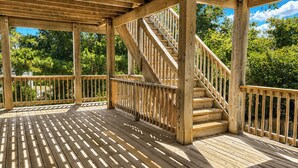 Una terraza de madera con una escalera que lleva a un nivel superior, rodeada de árboles.