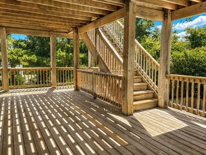 Une terrasse en bois avec un escalier menant à un niveau supérieur, le tout entouré d’arbres.