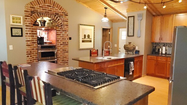 A kitchen with a brick oven, wooden cabinets, and a dining area with chairs.