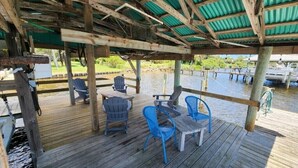 Une terrasse en bois avec des sièges extérieurs, un espace abrité et des bateaux en arrière-plan.