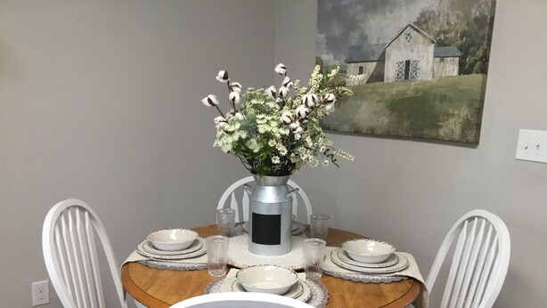 A dining table with white chairs, a vase with flowers, and a painting on the wall. - Adorable “Hudson Hideaway Cottage” (Hudson)