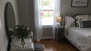 A bedroom with a bed, bedside table, lamp, and a mirror. - Adorable “Hudson Hideaway Cottage” (Hudson)