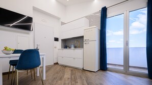 A modern kitchen with white cabinets, a white refrigerator, and a dining area with a blue chair and table. - Villa In Bed Blue Suite Balcony (Campania)