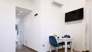 A modern room with a white table, blue chairs, a flat-screen TV, and a door. - Villa In Bed Blue Suite Balcony (Campania)
