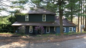 Une maison à deux étages avec un porche, entourée d’arbres et bordée d’une allée en gravier.