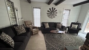 Un salon comprenant un canapé, deux fauteuils, une table basse et des rideaux à motifs.