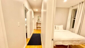 A narrow hallway with wooden flooring leading to a bed with white bedding. - North End, Lil Italy, TD Garden (Boston)