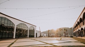A spacious courtyard with a modern building featuring large glass windows and a series of arches. - Hacienda Viga 2020 Hotel (Cuatro Ciénegas)