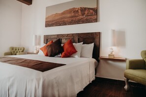 A neatly made bed with a wooden headboard, two bedside lamps, and a green armchair. - Hacienda Viga 2020 Hotel (Cuatro Ciénegas)