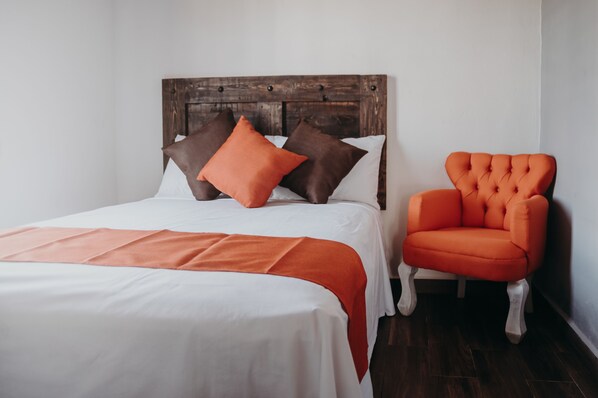 A neatly made bed with a wooden headboard, a bright orange chair, and a white bedspread. - Hacienda Viga 2020 Hotel (Cuatro Ciénegas)