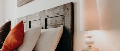 A bed with a wooden headboard, white and orange pillows, and a bedside table with a lamp.