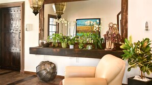 A reception area with a wooden reception desk, a mirror, a statue, and various potted plants. - Hacienda Viga 2020 Hotel (Cuatro Ciénegas)