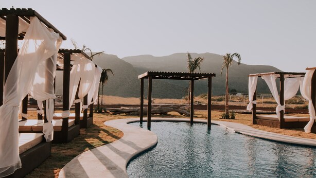 A pool area with a pergola and white drapes, surrounded by a desert landscape and mountains. - Hacienda Viga 2020 Hotel (Cuatro Ciénegas)