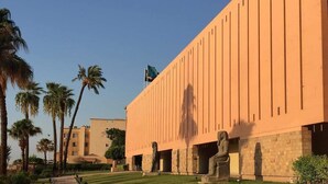A building with a long, straight facade, palm trees, and a paved walkway. - Orient star hotel (Luxor)