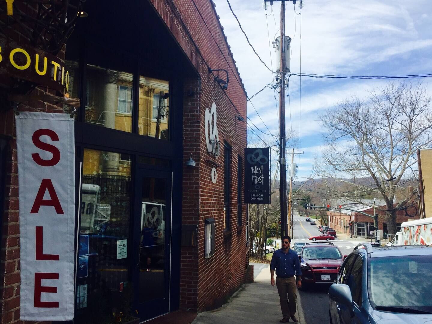 A storefront with a 'SALE' sign, a 'West First' sign advertising lunch and dinner, and a brick building facade.