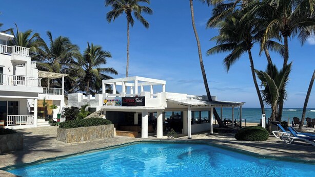 A pool area with a clear view of the ocean, palm trees, and a building with a sign reading 'La Mesa Tahiti.' - Closest Condo to Sand on Kite Beach | 2 Decks | Ocean Views (Cabarete)