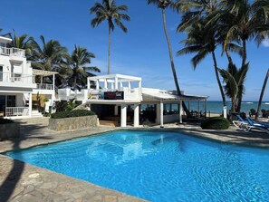 Un espace piscine offrant une vue dégagée sur l’océan, les palmiers et un bâtiment sur lequel on peut lire l’inscription « La Mesa Tahiti ».