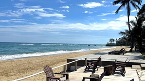 A beachside deck with Adirondack chairs and a wooden deck overlooking the ocean. - Closest Condo to Sand on Kite Beach | 2 Decks | Ocean Views (Cabarete)