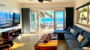 A modern living room with a large flat-screen TV, a sofa, a coffee table, and a view of the ocean through large windows. - Closest Condo to Sand on Kite Beach | 2 Decks | Ocean Views (Cabarete)
