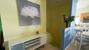 A room with a white console table, a painting of a flower, a vase with flowers, a chair, and a kitchen area with wooden cabinets and a stove. - Scenic 2 bed, 1.5 bath condo with river views on St. Clair River - U2 (Marysville)
