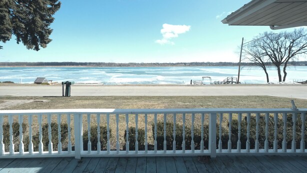 A view from a porch with a white railing, overlooking a frozen body of water and a distant shoreline. - Scenic 2 bed, 1.5 bath condo with river views on St. Clair River - U2 (Marysville)
