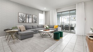 A modern living room with a grey sofa, a coffee table, and a green ottoman. There is a glass door leading to a balcony. - Private Pool, BBQ, Themed Suites, PS5 Just Close to Disney (Four Corners)