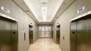 Atrio moderno con due ascensori, pavimento lucido e lampadario decorativo.