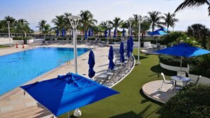 Una piscina amb gandules i ombrel·les, envoltada de palmeres i un cel serè.
