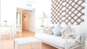 Un sofà blanc amb coixins florals, una taula de cafè blanca i una decoració de paret calada en una habitació lluminosa amb sòl de rajola.